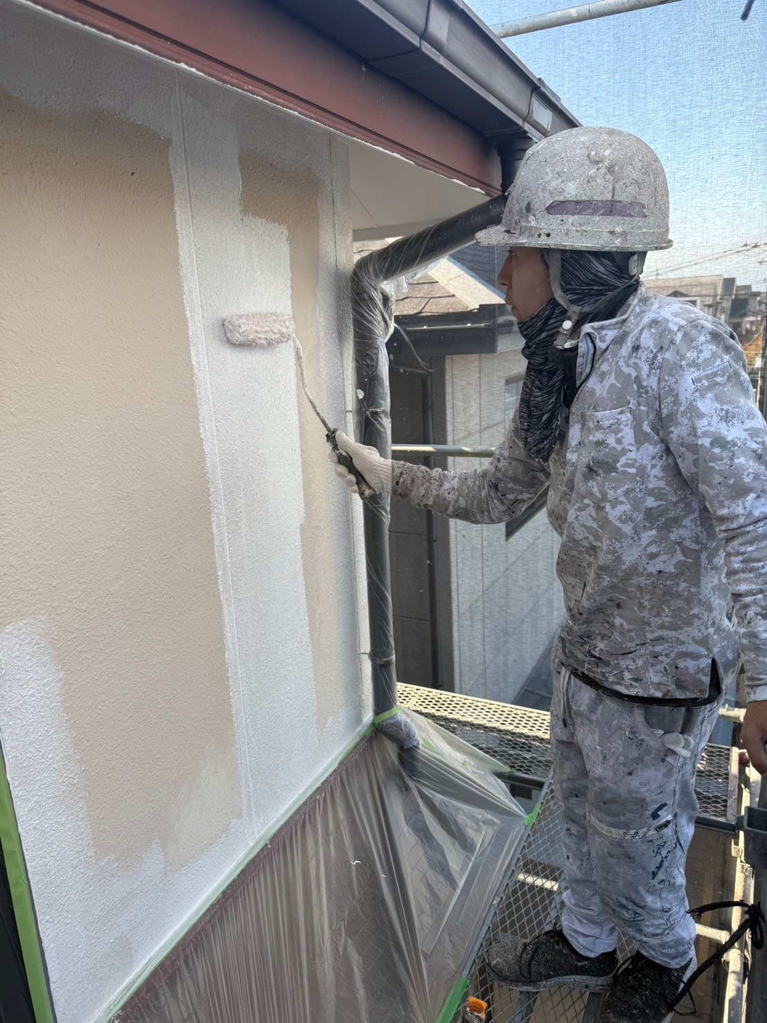 白い外壁をローラーで塗装する作業