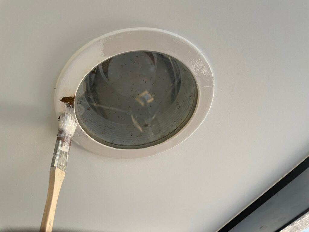 軒天の照明器具まわりを刷毛で塗装している様子